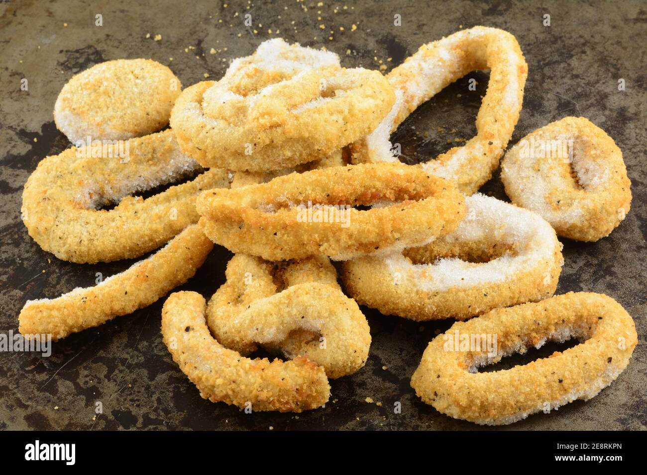 Frozen breaded calamari rings with ice crystals on weathered baking pan