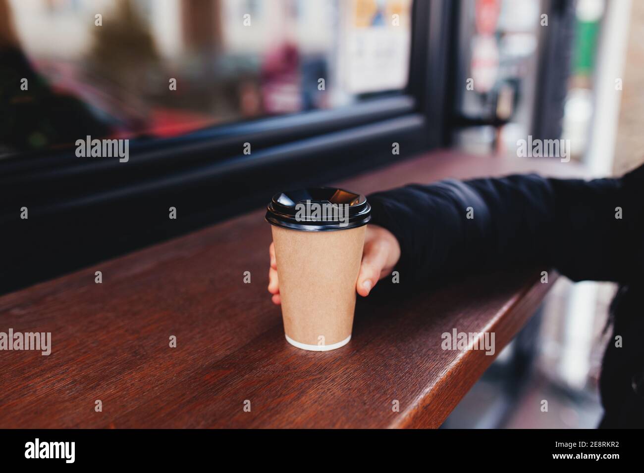 Girl holds a paper cup of coffee in hand near cafe Stock Photo