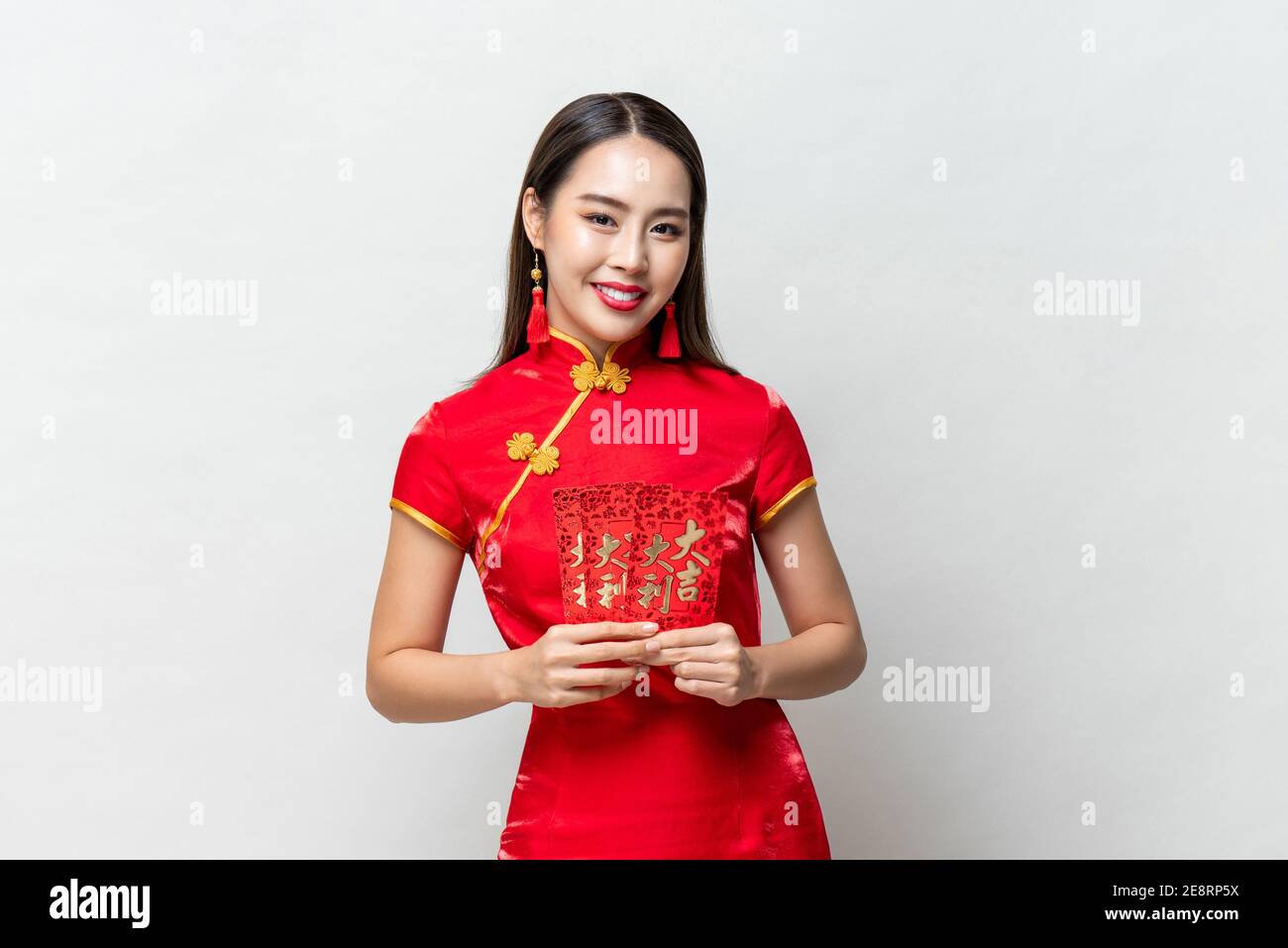 Smiling happy Asian woman in traditional oriental costume holding red envelopes or Ang Pao in light gray background for Chinese new year concepts,  te Stock Photo