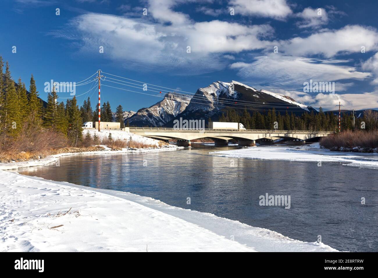 Trucks Passing over Alberta Bow River Bridge on Trans Canada Highway 1 or Highway One with Distant Snowy Peaks of Canadian Rocky Mountains on Horizon Stock Photo