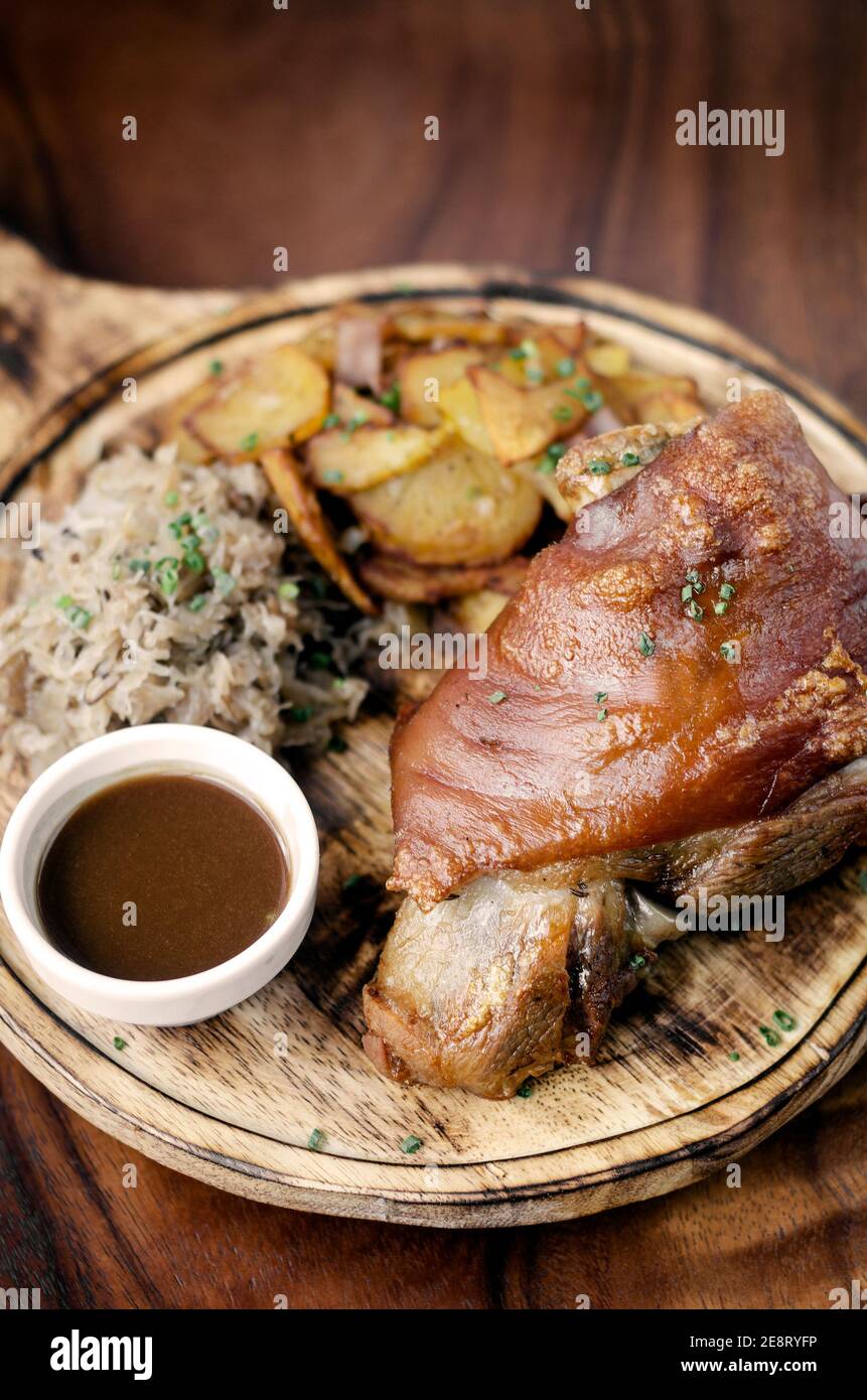 SCHWEINSHAXE traditional german pork knuckle with sauerkraut and potatoes bavarian meal on rustic wood background Stock Photo