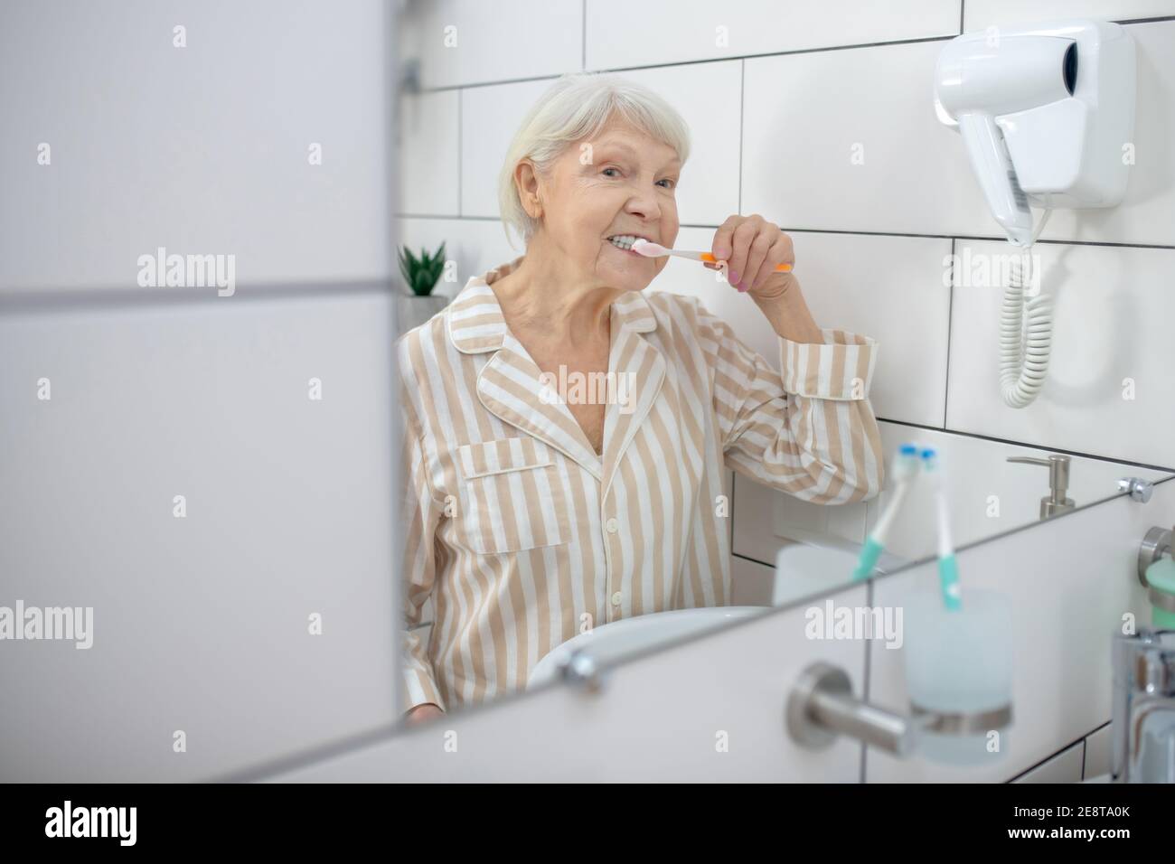 Elderly woman brushing her teeth in the bathroom Stock Photo