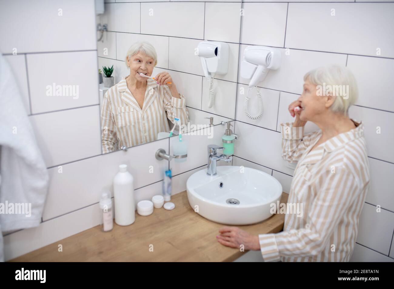 Elderly woman brushing her teeth in the bathroom Stock Photo