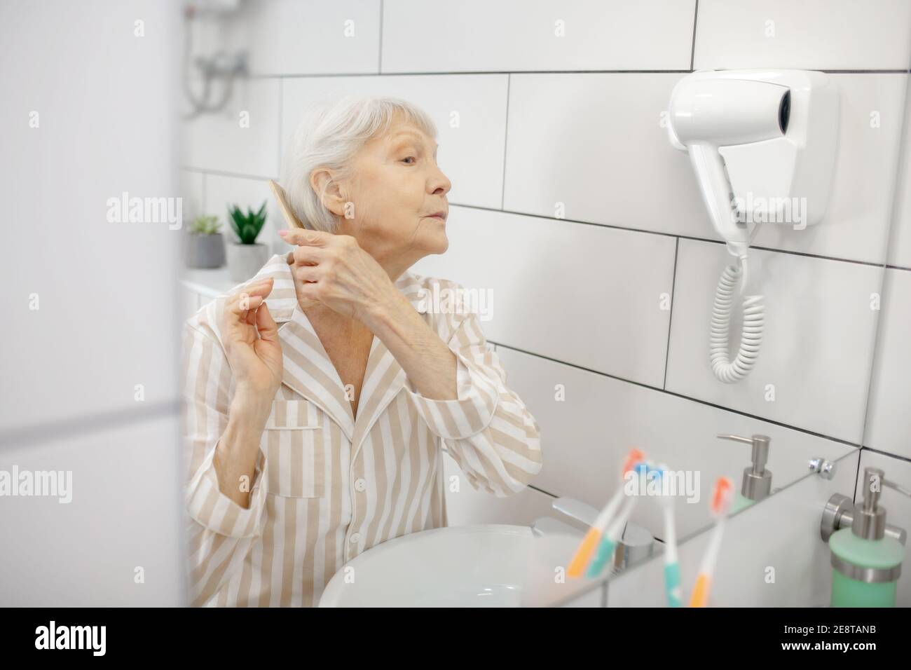 Gray-haired woman brushing her hair in the bathroom Stock Photo