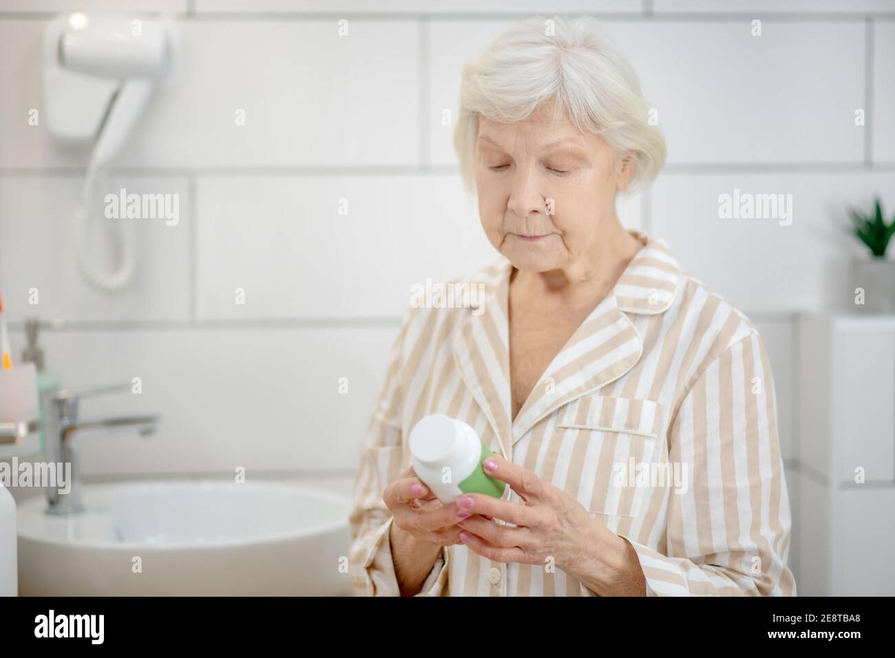 Short-haired old lady holding a bottle with vitamins in her hands Stock Photo