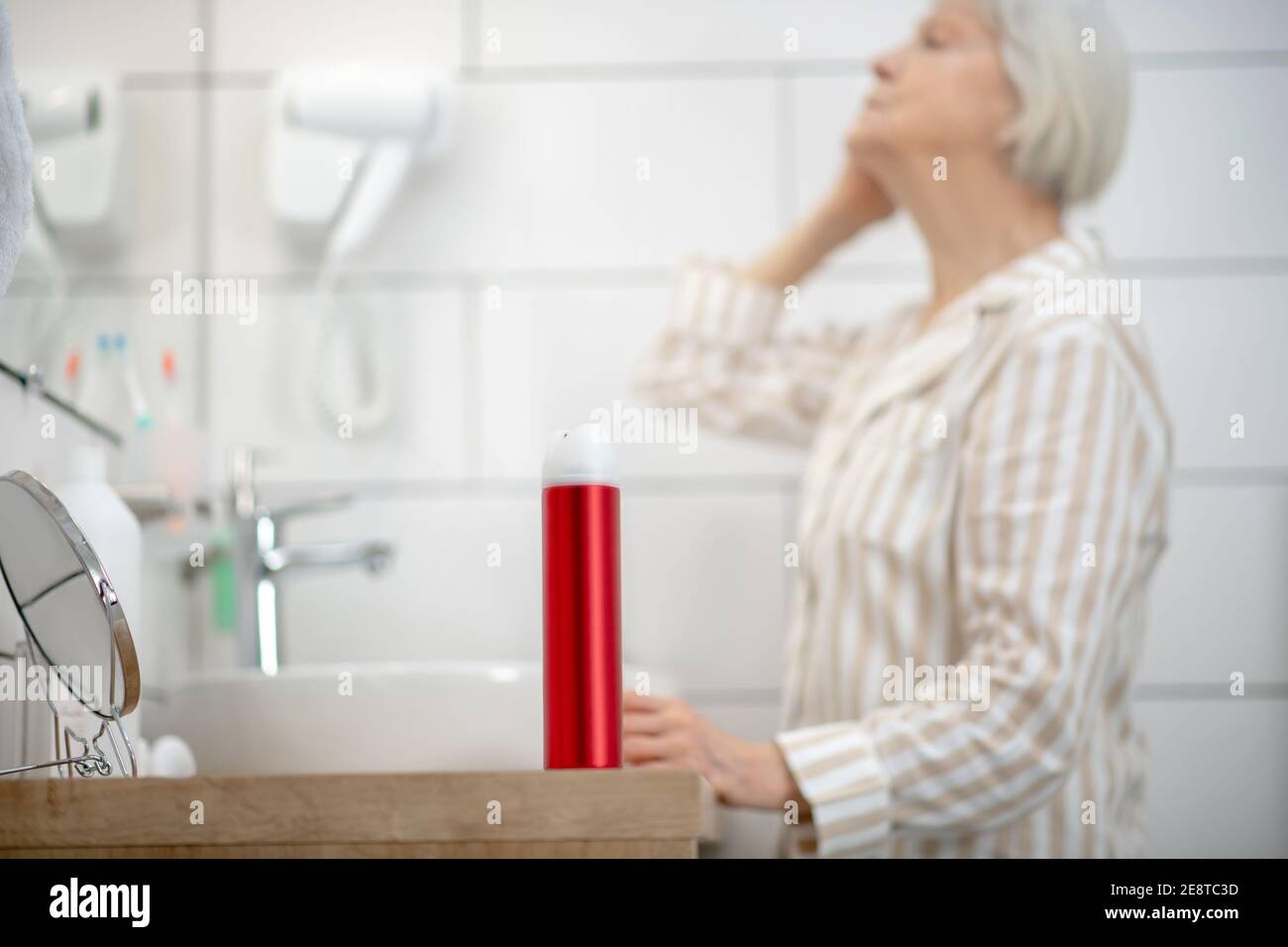 Gray-haired woman in pajama doing hair in the bathroom Stock Photo