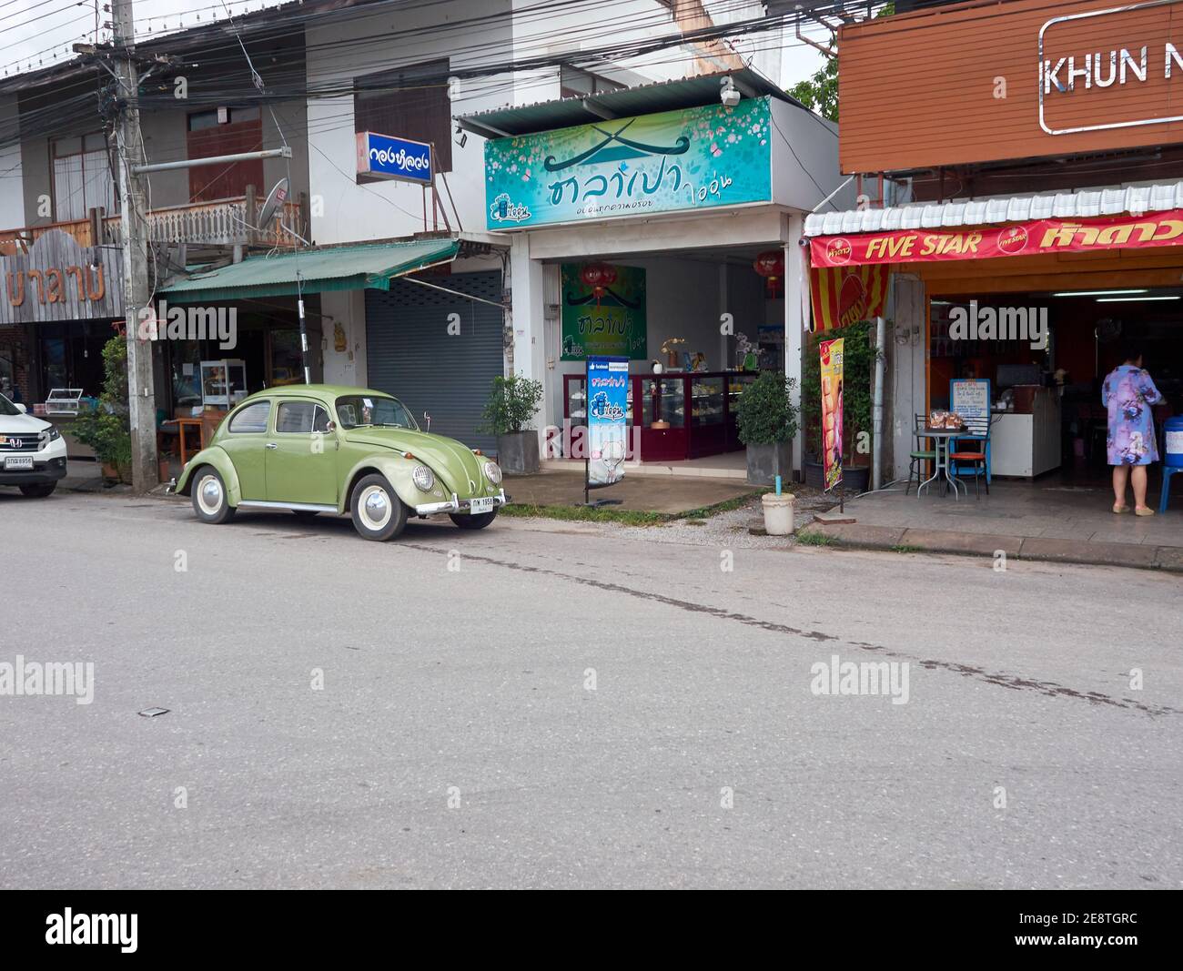 A green volkswagen beetle is parked on the side of the road in front of the shop Stock Photo