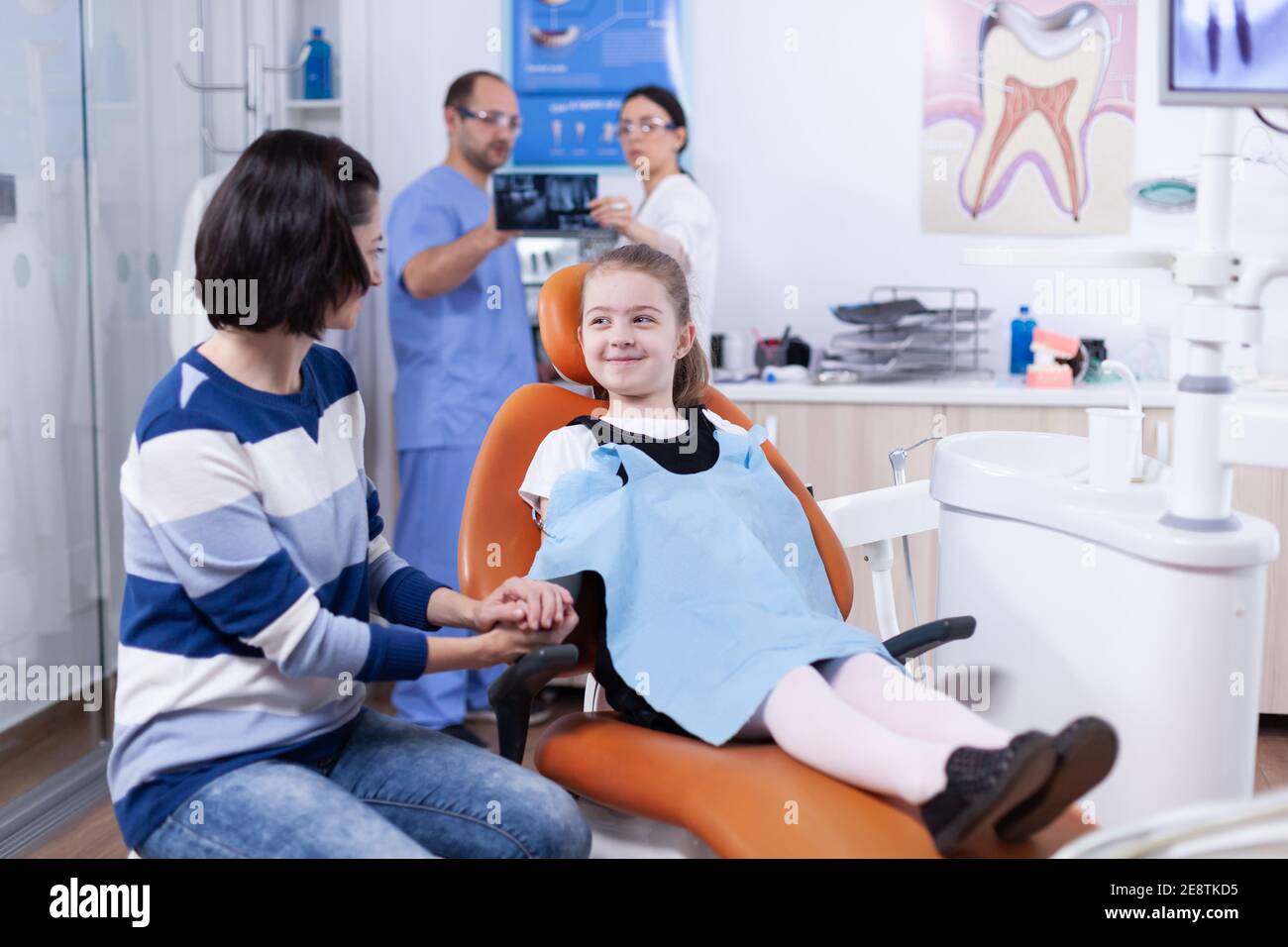 Happy little girl wearing dental bib in dentist office holding parent hand waiting tooth