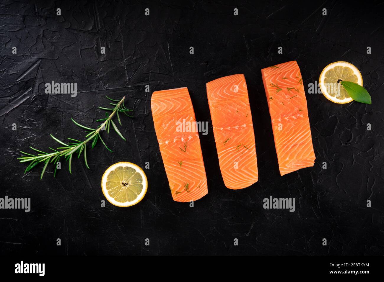 Salmon with lemons and herbs, overhead flat lay shot on a black ...