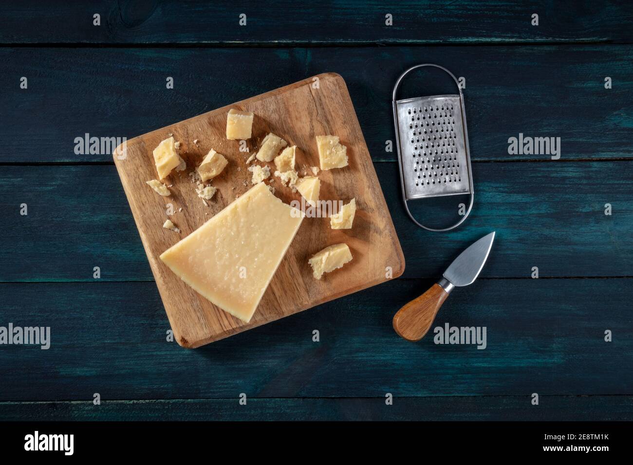 https://c8.alamy.com/comp/2E8TM1K/crumbled-parmesan-cheese-with-a-knife-and-a-grater-shot-from-above-on-a-dark-wooden-background-2E8TM1K.jpg
