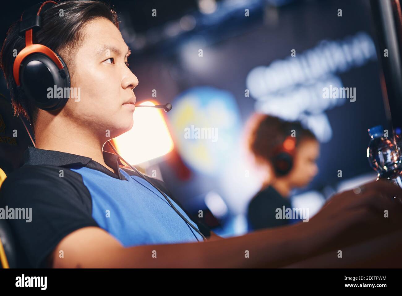 Side view of a focused asian guy, male cyber sport gamer wearing headphones playing online video games, participating in eSports tournament while sitting in gaming club or internet cafe Stock Photo