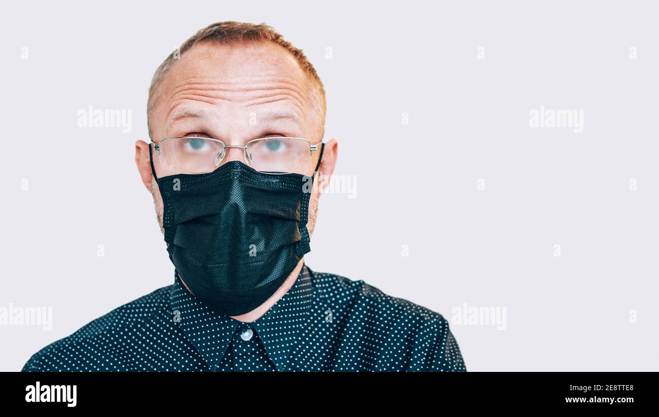 Portrait of surprised man in black facial mask during a COVID-19 world pandemic looking at camera. Self-protection and stop virus spreading measures c Stock Photo