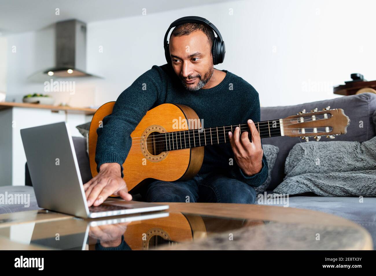 Black man playing the guitar at home and using a laptop Stock Photo