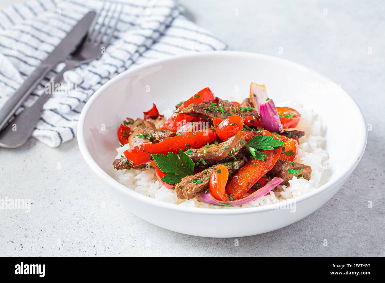 Fried pieces of beef with vegetables and rice in a white plate. Stir fry beef with peppers and onions, served with rice. Stock Photo
