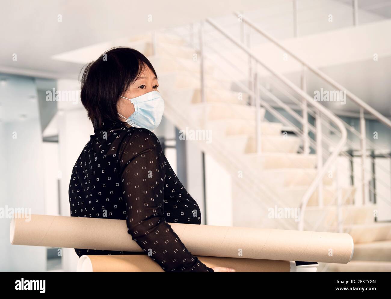 Mature asian woman with a surgical mask holding cardboard blueprint tubes  on an out of focus office background. Selective focus. Safety concept Stock  Photo - Alamy