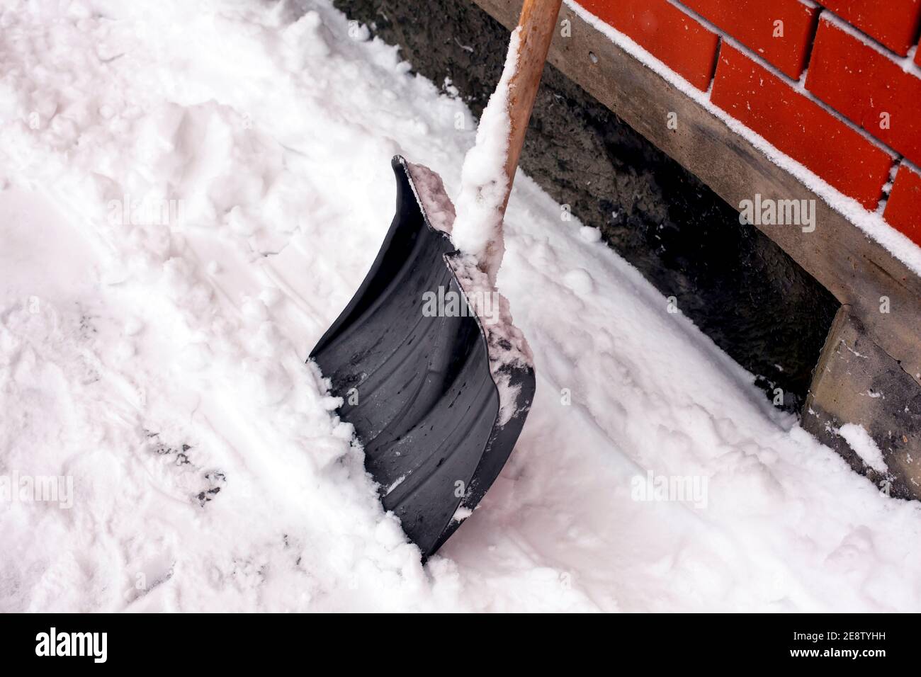 Snow shovel standing in snow near brick wall outdoors. Close-up Stock Photo