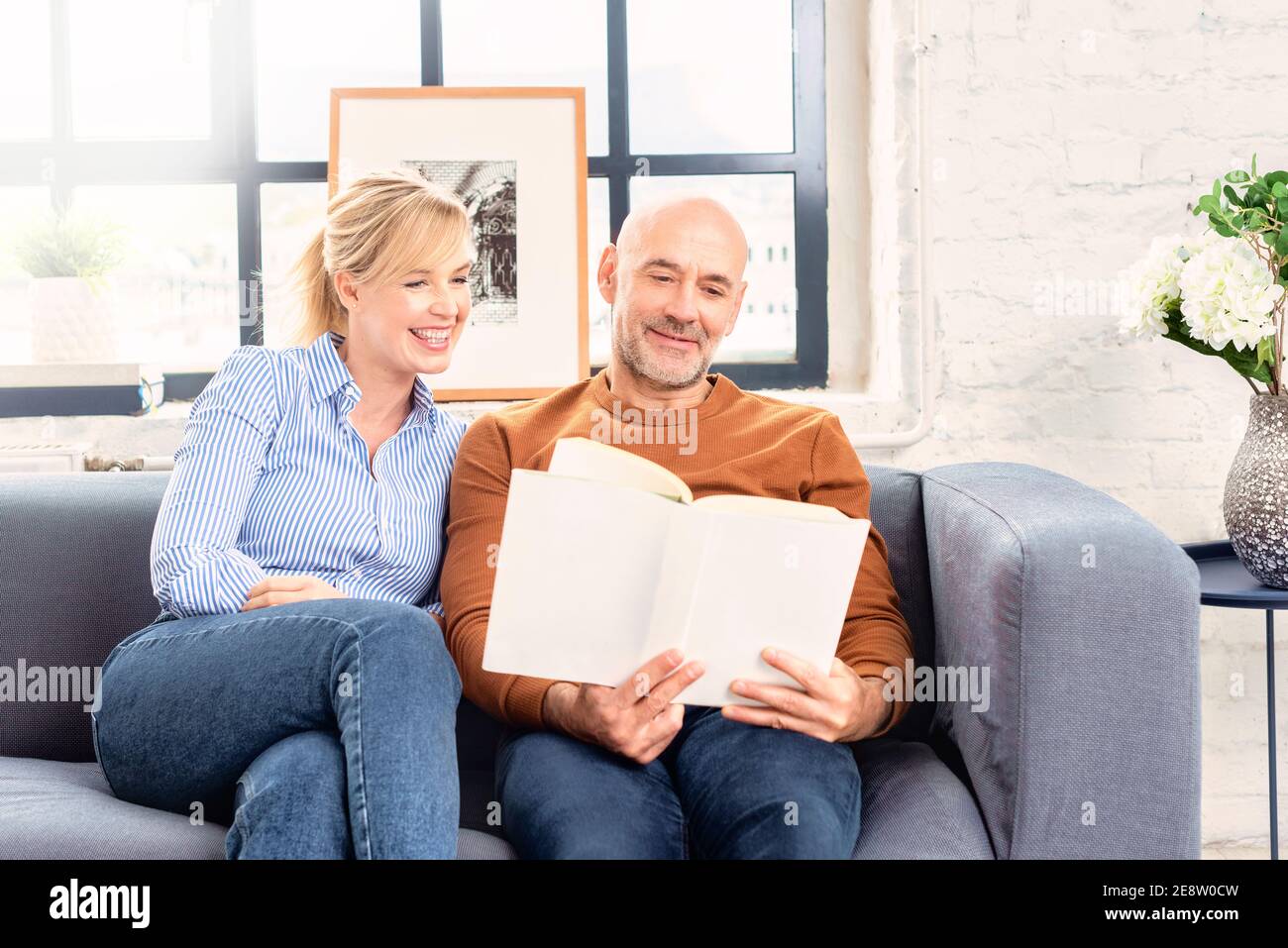 Shot of happy couple sitting on couch at home and reading book together while relaxing at home. Stock Photo