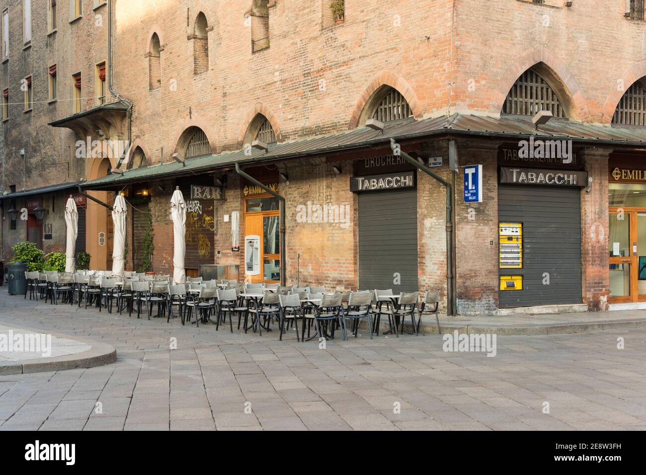 The Emilian Cafe and tobacconist shop in an old buidling on a street corner in Bologna Italy, closed with empty chairs and tables outside. Stock Photo
