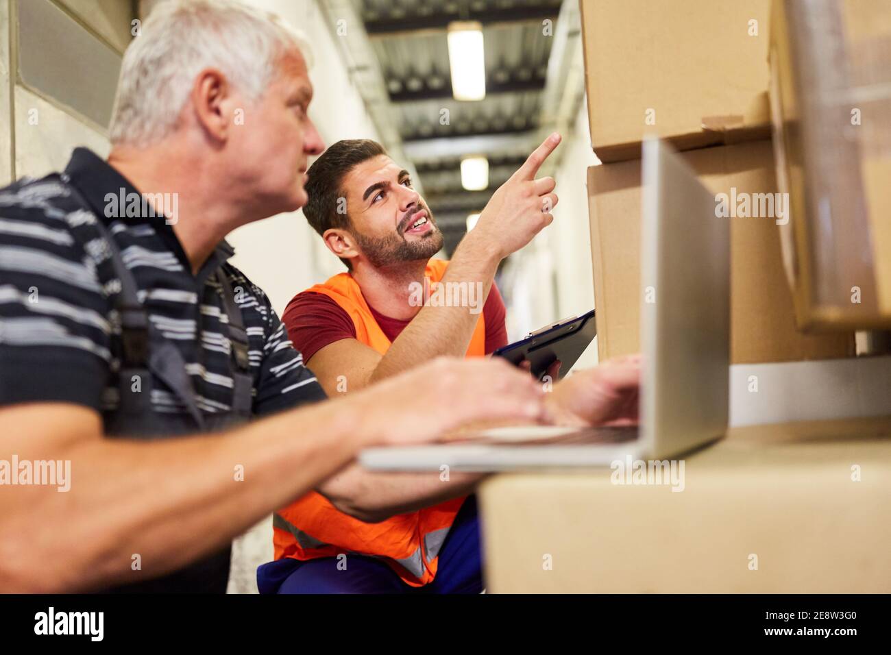 Two warehouse workers at laptop PC with parcels in the online shop ...