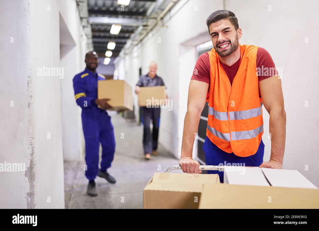 Smiling worker with safety vest pushes packages on push carts into the warehouse Stock Photo