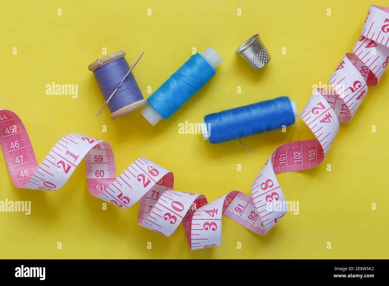 Spools of thread, a needle, a thimble and a measuring tape on a yellow background. View from above. Stock Photo