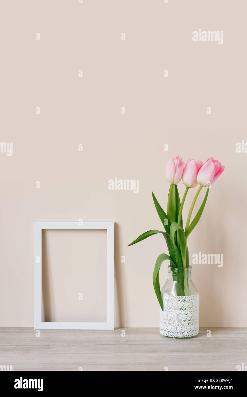 Home interior with decor elements. Mockup with a white frame and pink tulips in a vase on a light beige background Stock Photo