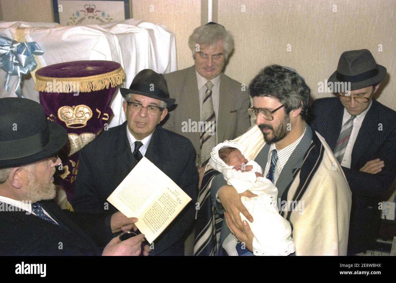 A father holds his eight day old son to received a blessing before the Brit Milah (circumcision procedure) in a Birmingham home. Stock Photo