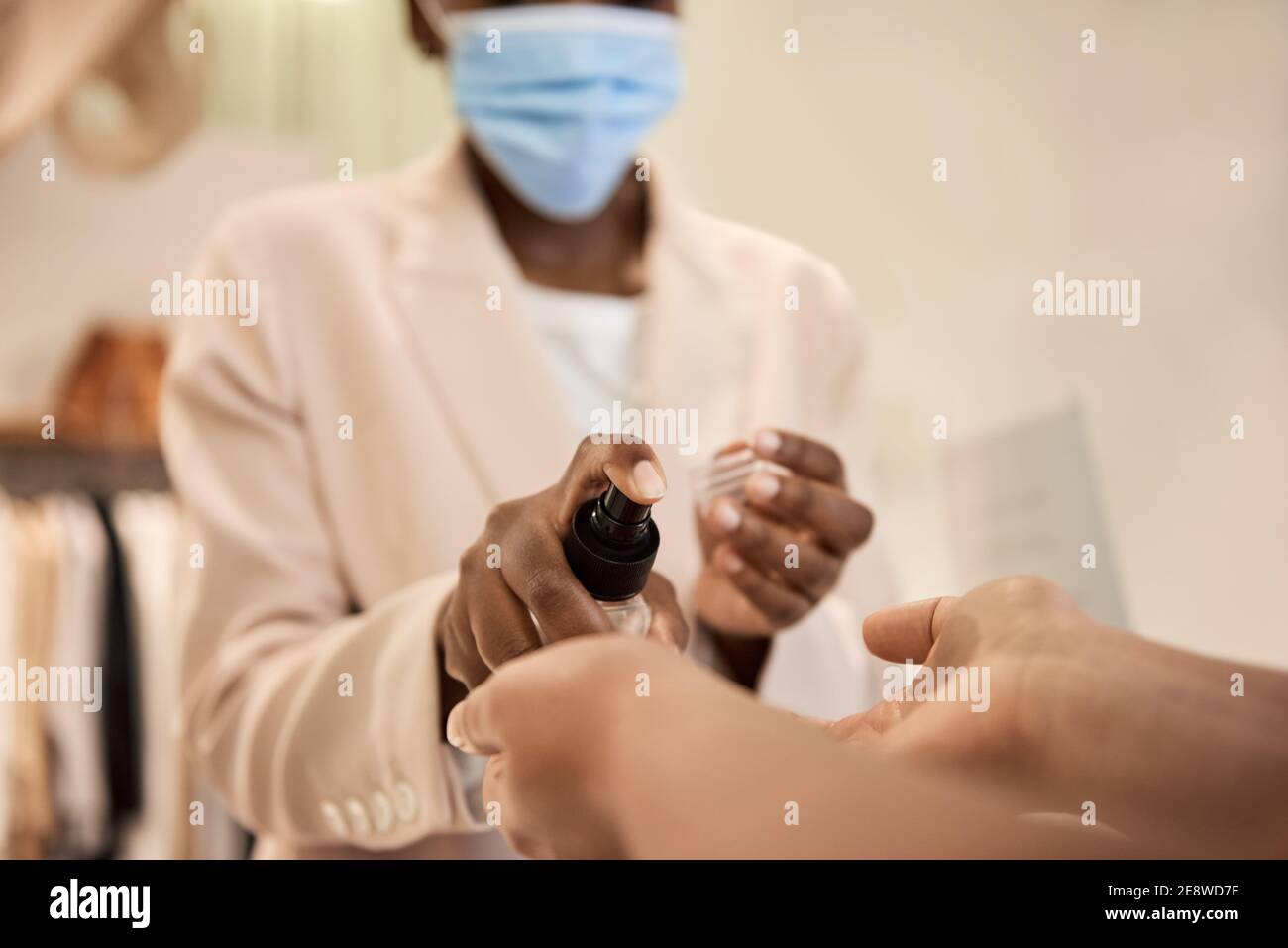 African American boutique owner spraying sanitizer on a customer's hands Stock Photo