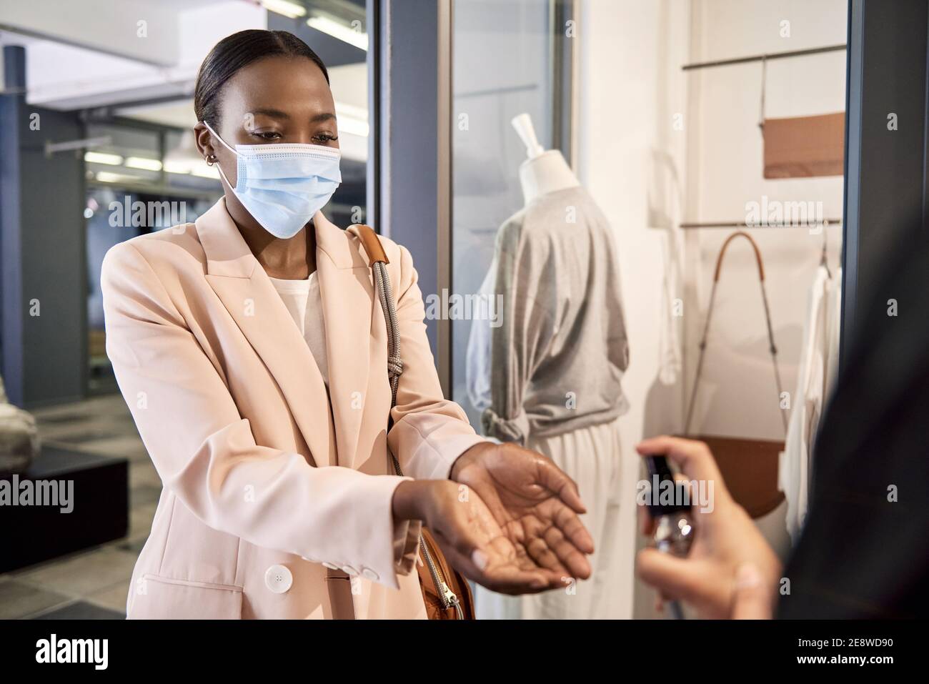 African American shop customer having sanitizer sprayed on her hands Stock Photo