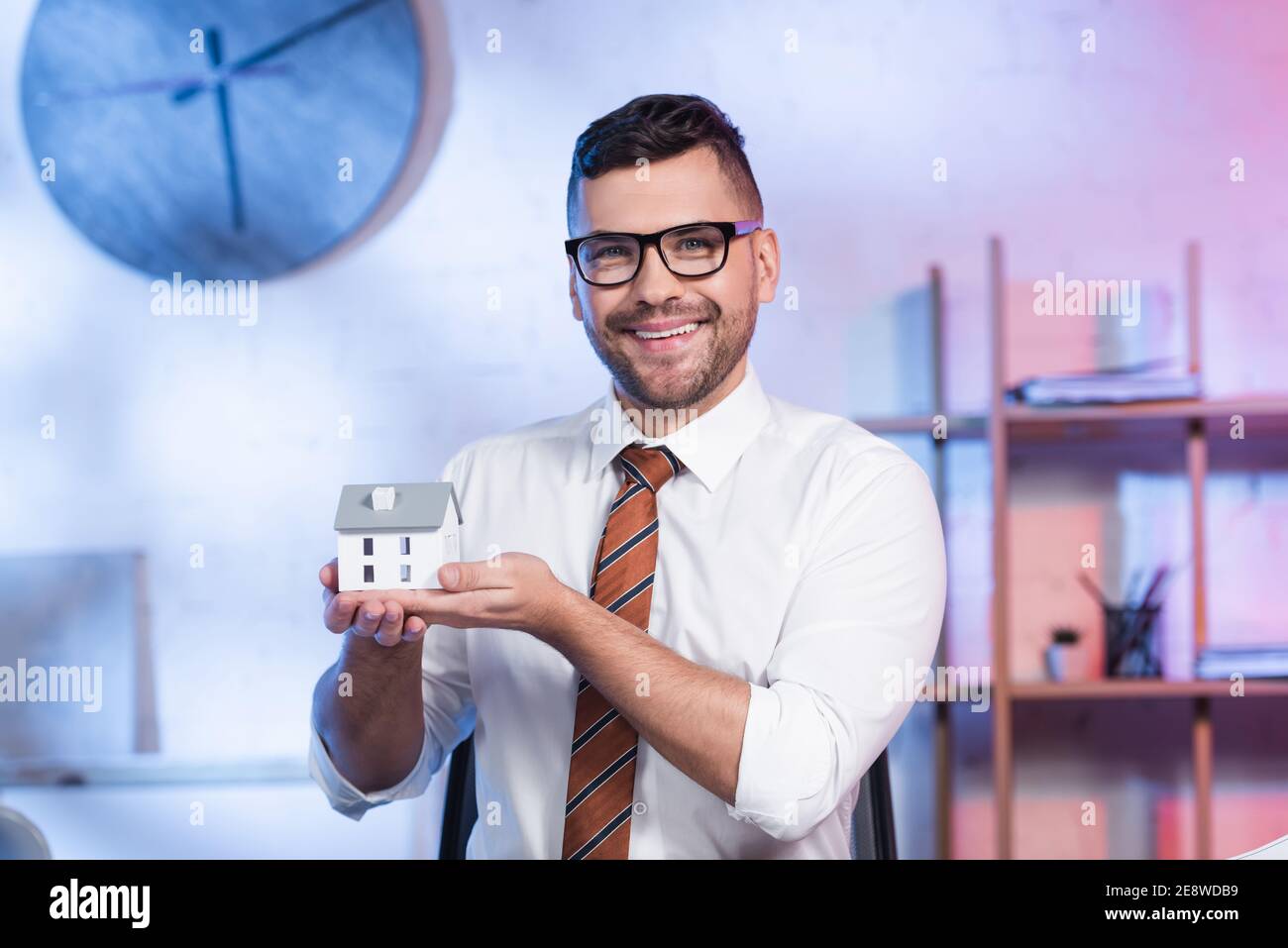 cheerful architect in eyeglasses holding house model and smiling at camera Stock Photo