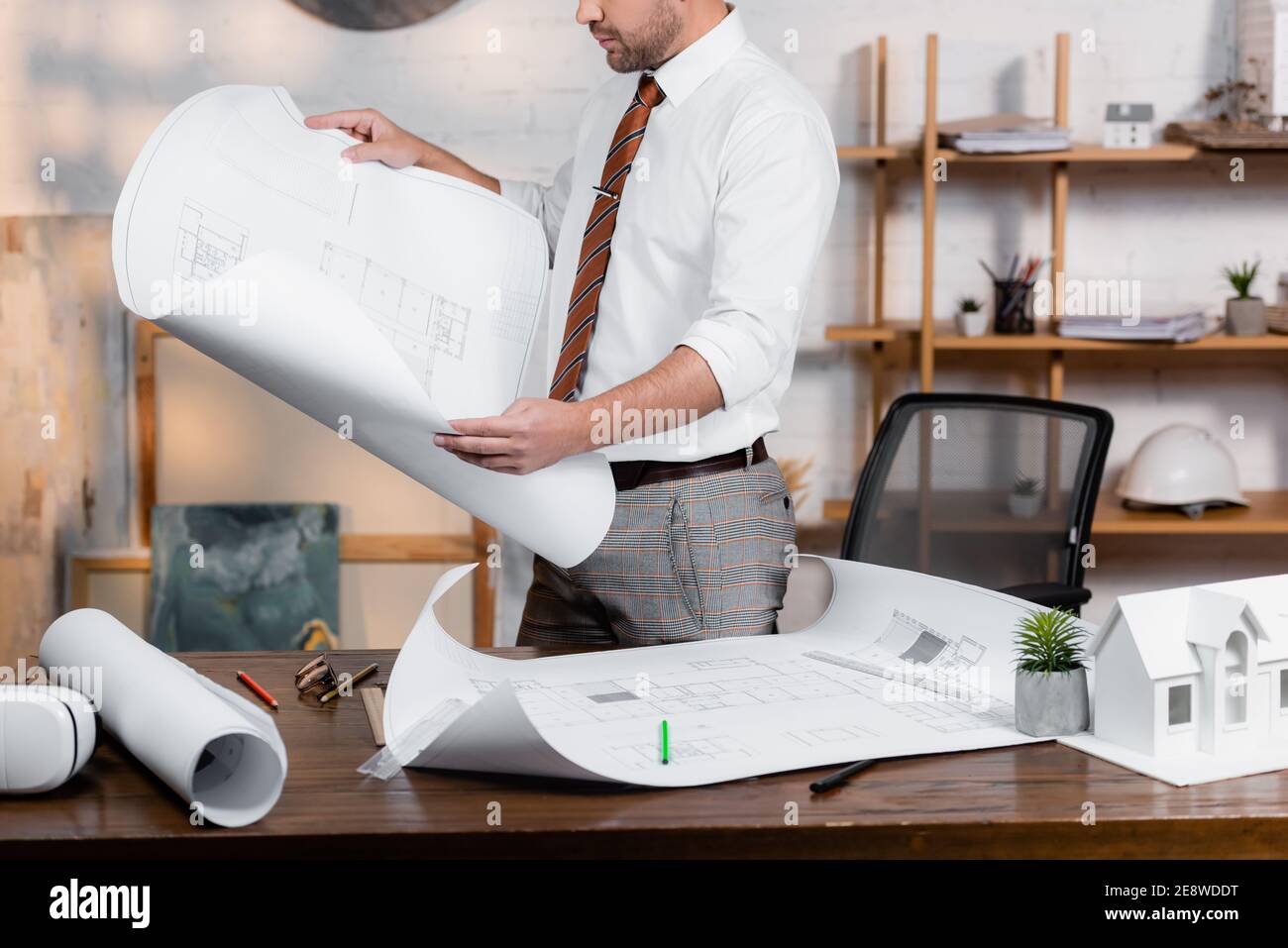 cropped view of architect holding blueprint near plans and house model on desk Stock Photo