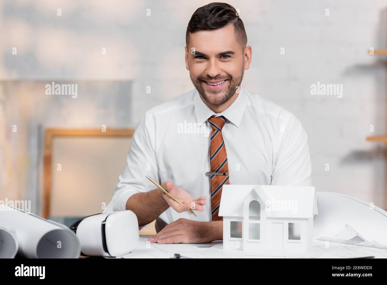 happy architect looking at camera while pointing at house model Stock Photo