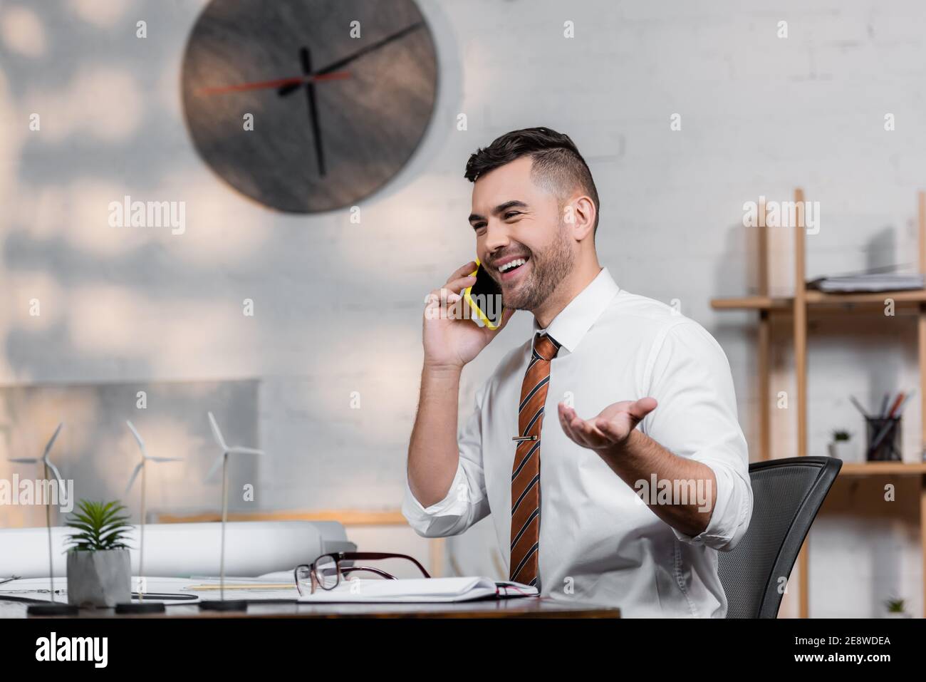 cheerful architect talking on smartphone at workplace near architectural project Stock Photo