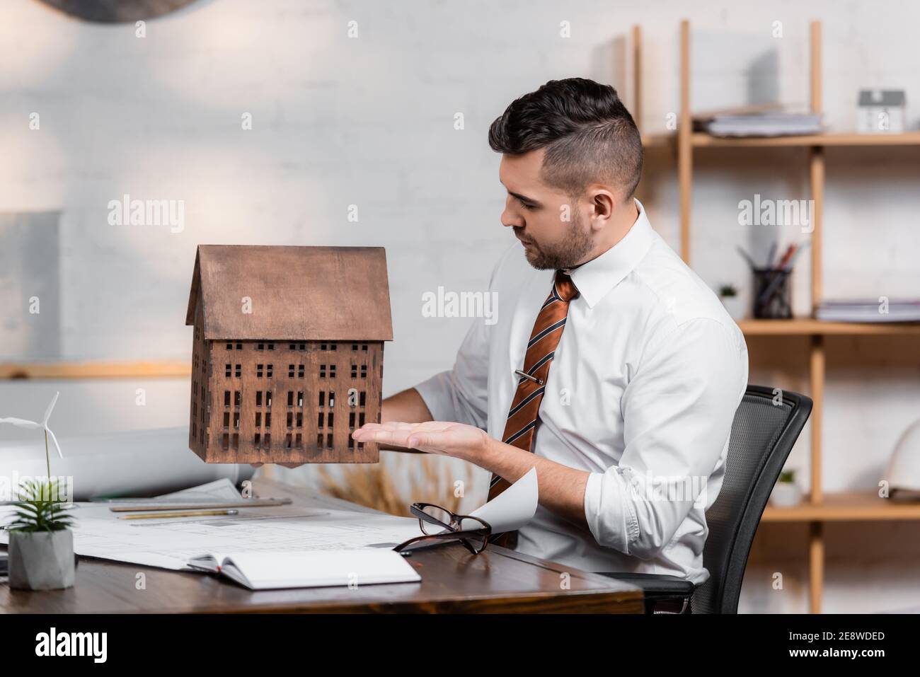 architect sitting at workplace and pointing with hand at house model Stock Photo