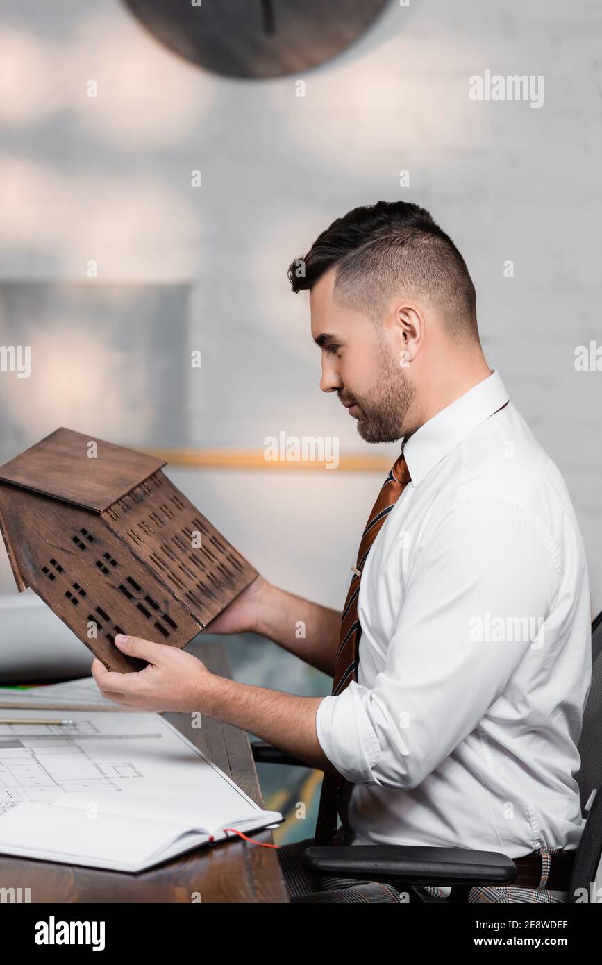 side view of architect holding house model while sitting at workplace Stock Photo