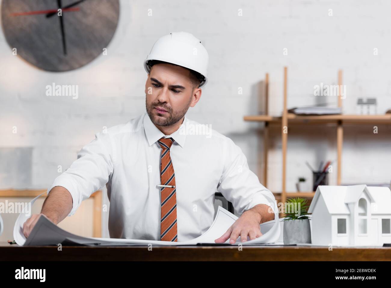 concentrated architect in helmet working on project near house model Stock Photo