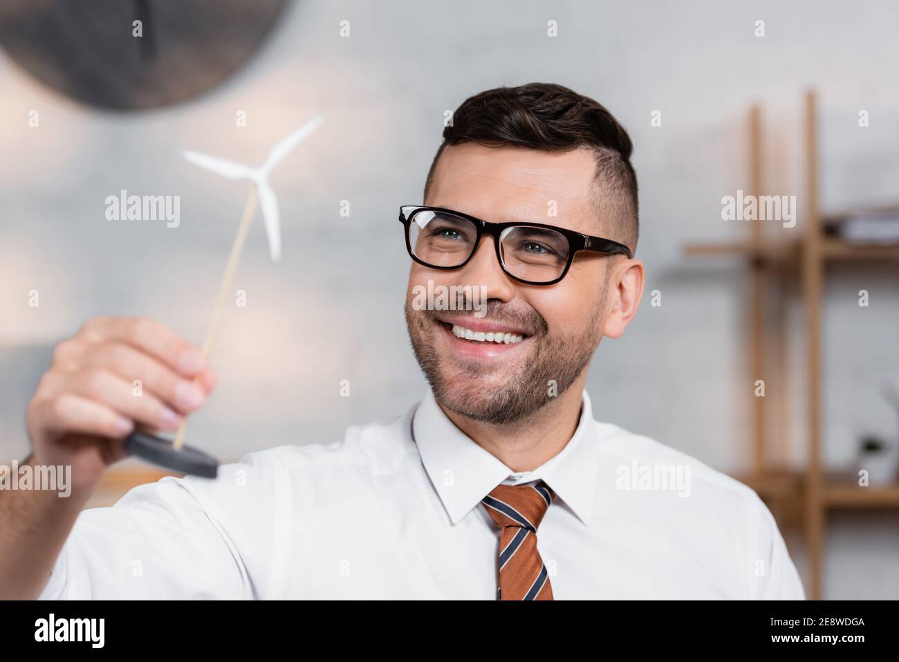 cheerful architect in eyeglasses smiling while holding model of wind turbine Stock Photo