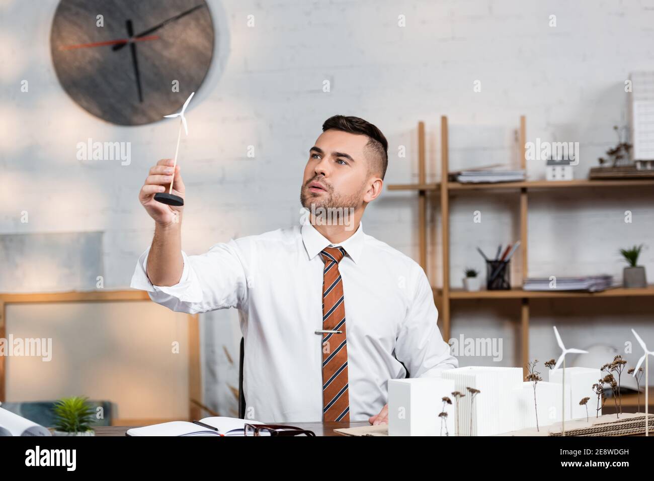 architect holding model of wind generator near architectural project at workplace Stock Photo