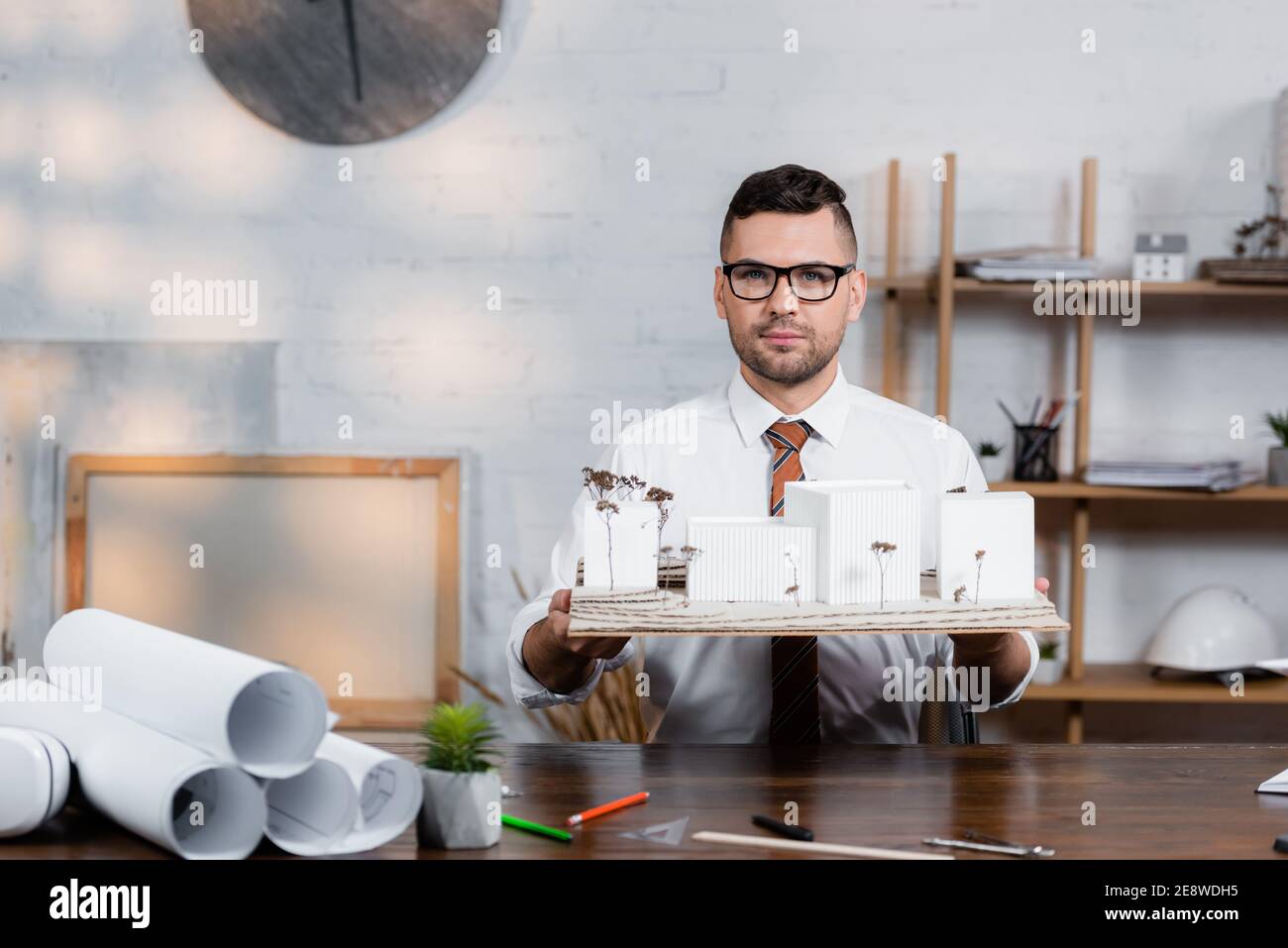 confident architect looking at camera while holding architectural ...