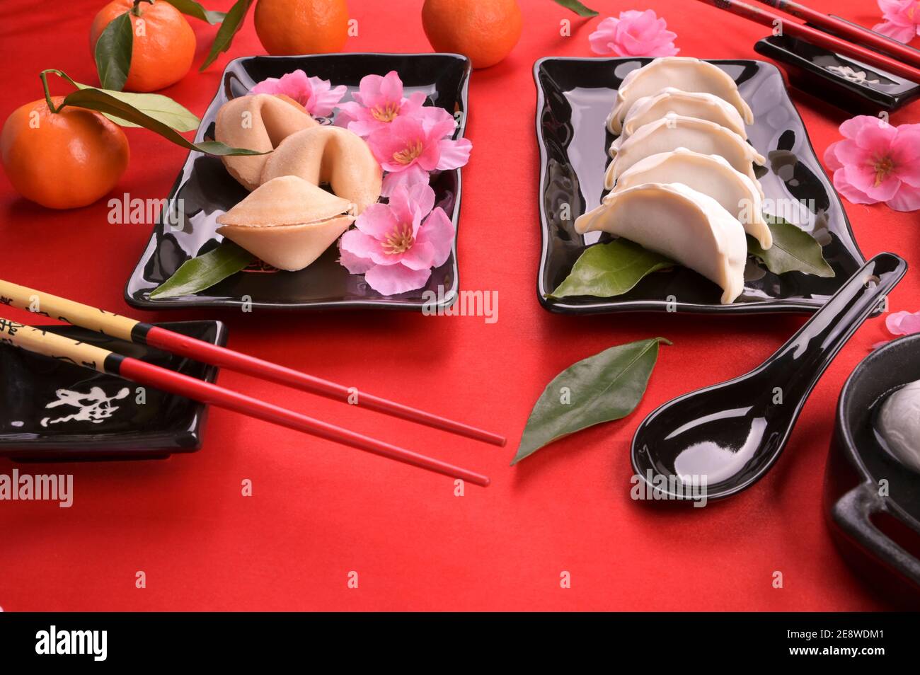 Festive oriental dinner. Chinese new year food and drink still life. Steamed dumpling, Tangyuan rice balls, fortune cookies on black plate and red background. High quality photo. Above Stock Photo