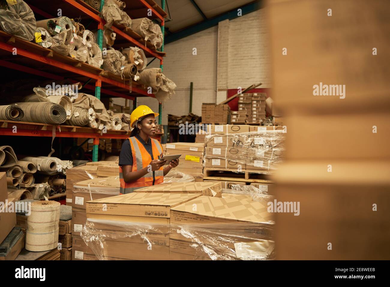 African female warehouse worker checking boxes using a digital tablet Stock Photo