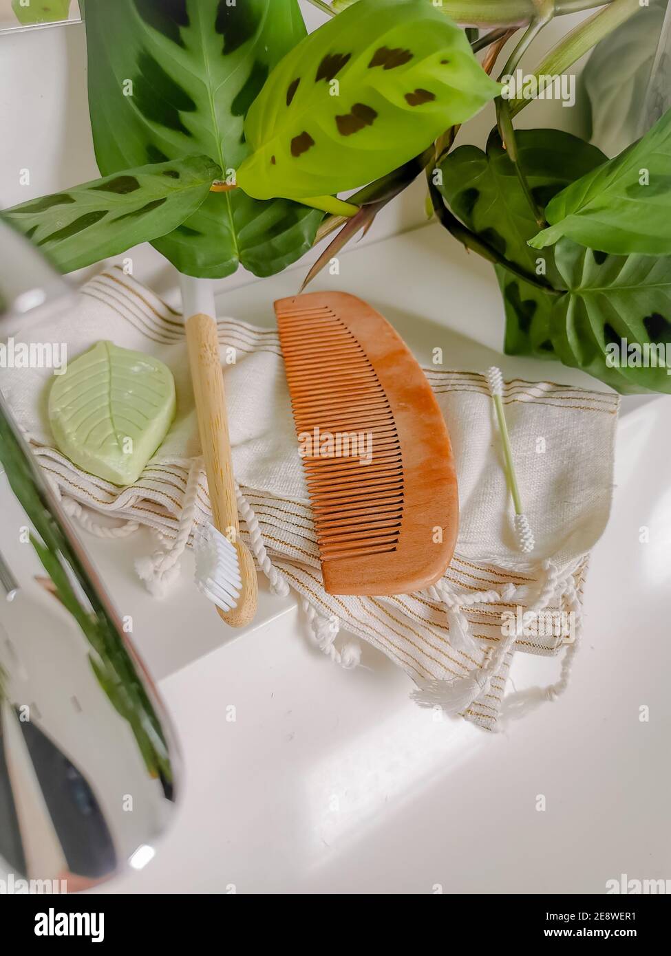 Plastic free and reusable personal care products such as silicone cotton swabs, bamboo toothbrush and comb, and a piece of soap on a bathroom counter. Stock Photo