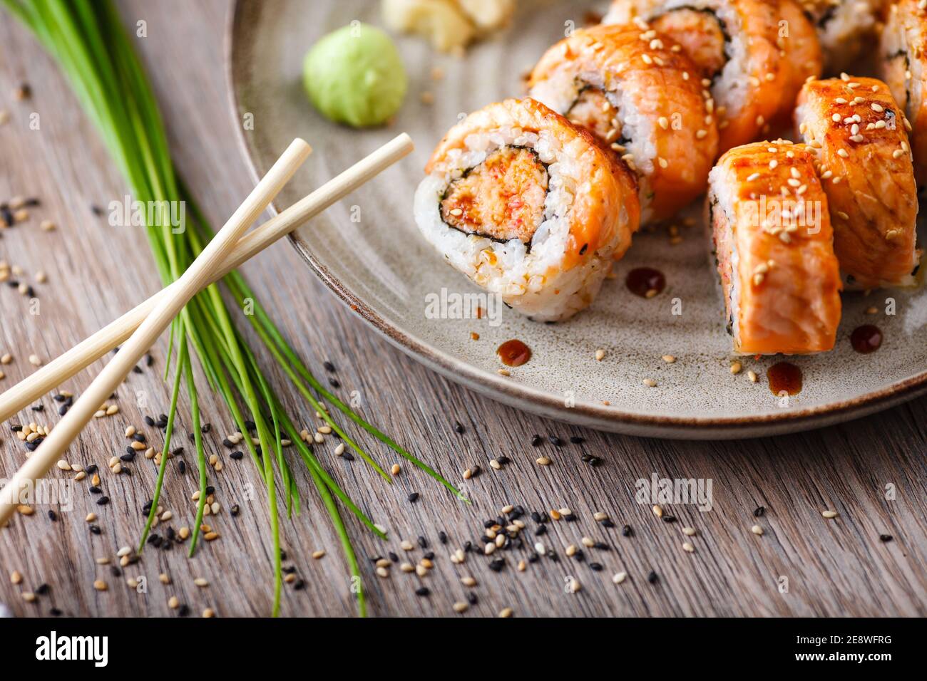 Baked sushi maki rolls with salmon, crab and spicy sauce on a plate with chopsticks, soy sauce, wasabi and ginger. Japanese traditional fish food clos Stock Photo