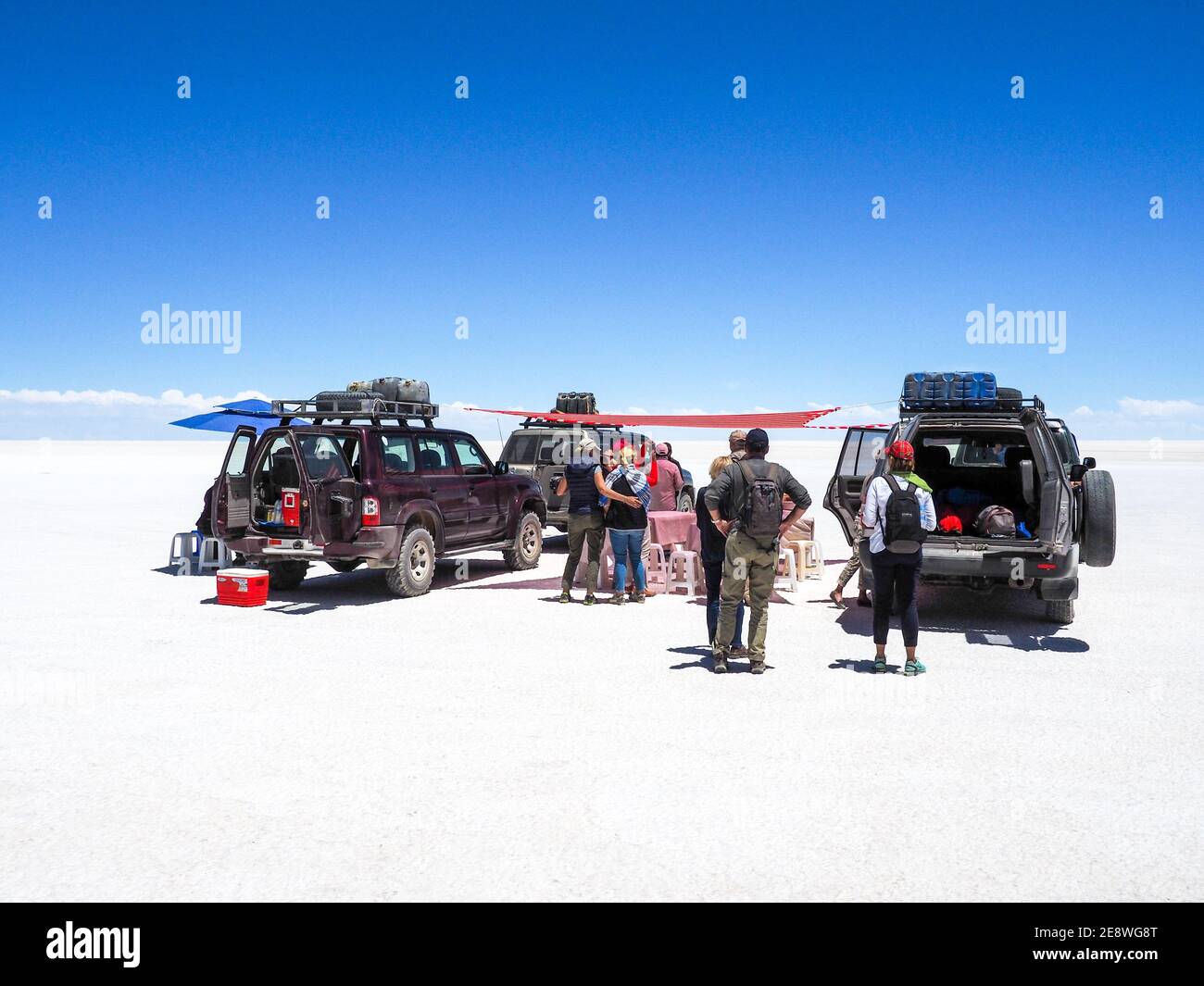 Tourists have lunch under a parasol next to their jeeps in the salt desert Uyuni, Bolivia Stock Photo