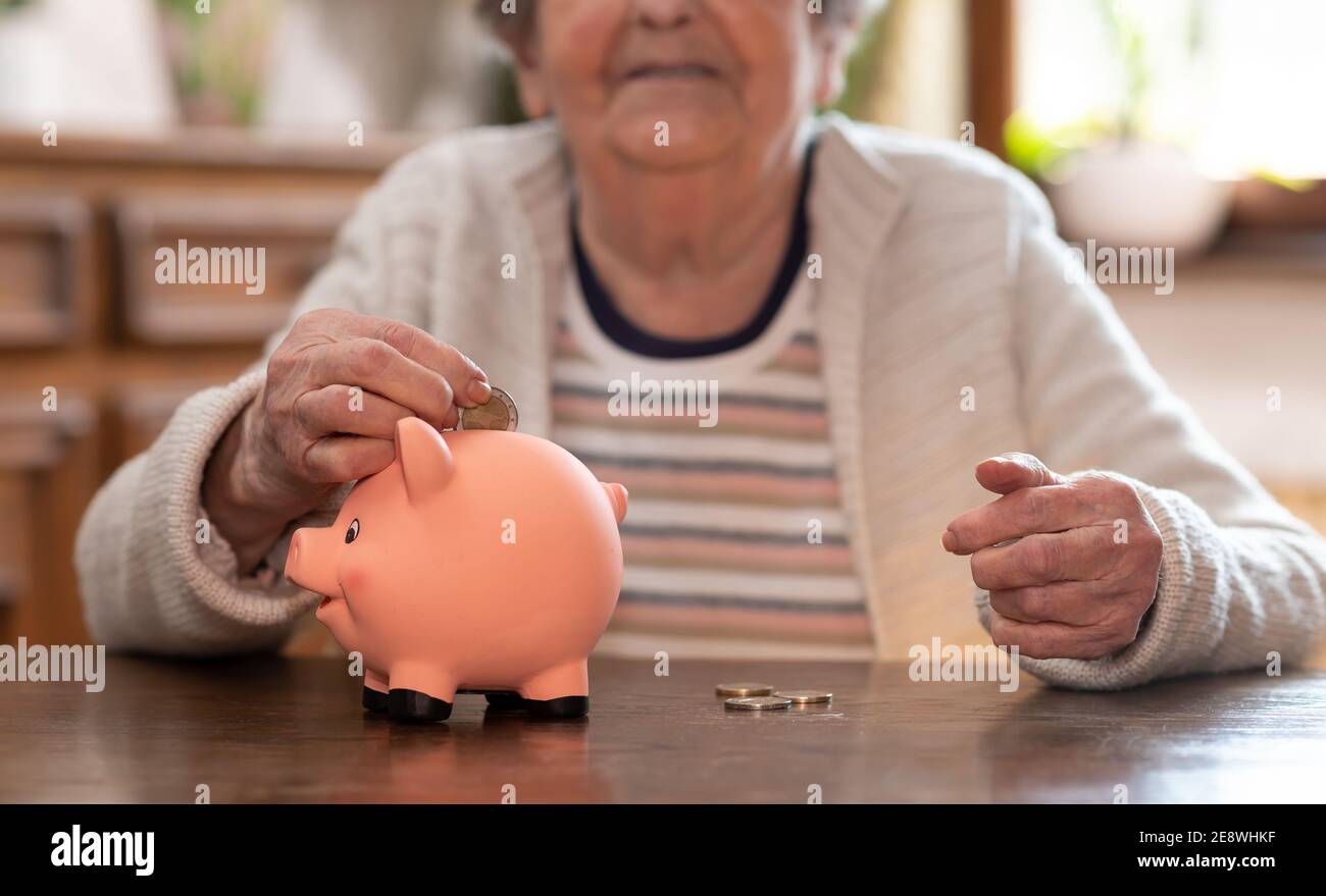Elderly woman putting a coin in a piggy bank Stock Photo - Alamy