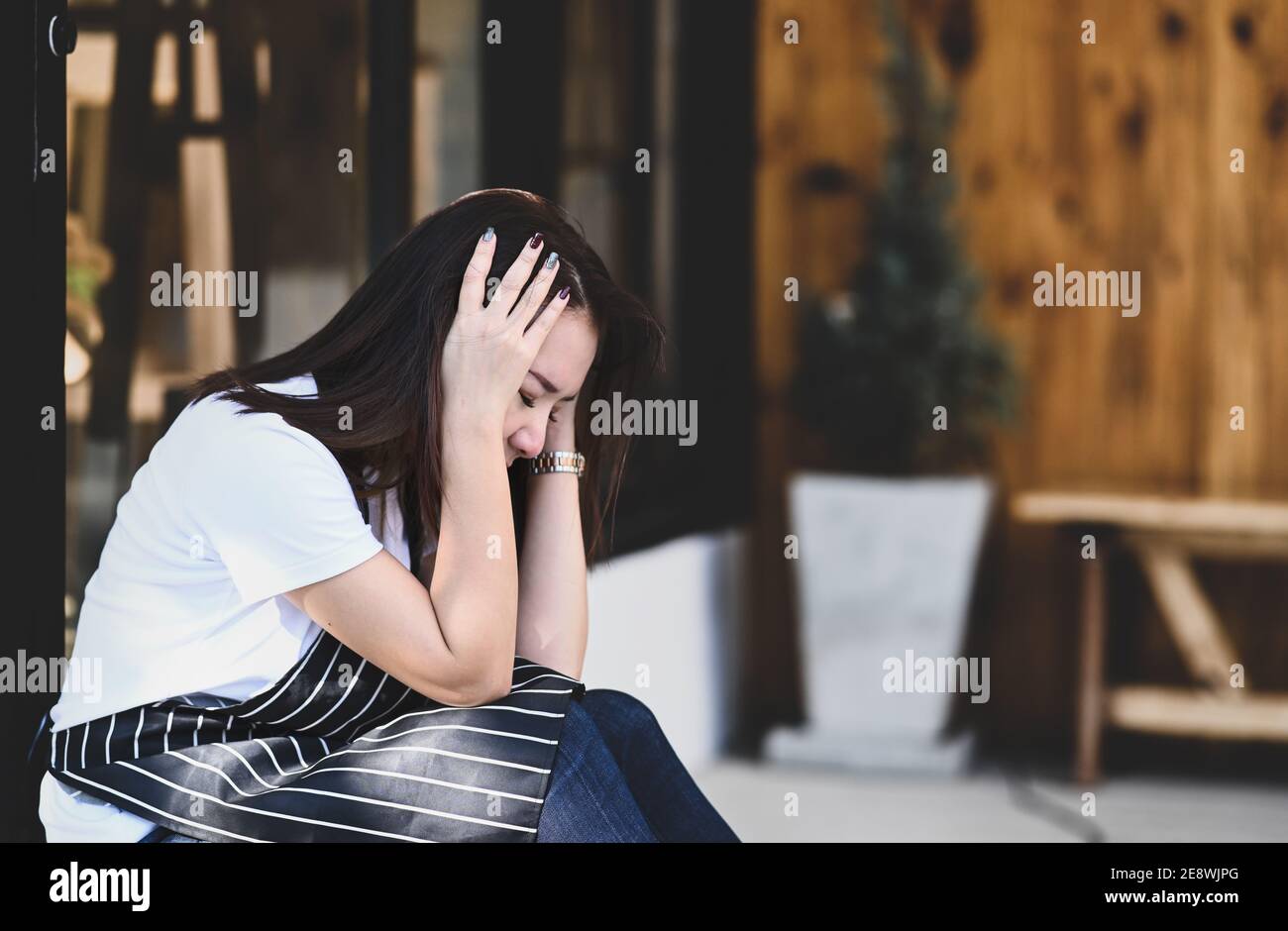 Young female coffee shop owner woman feeling stress or depress while sitting in front of her coffee shop. Stock Photo