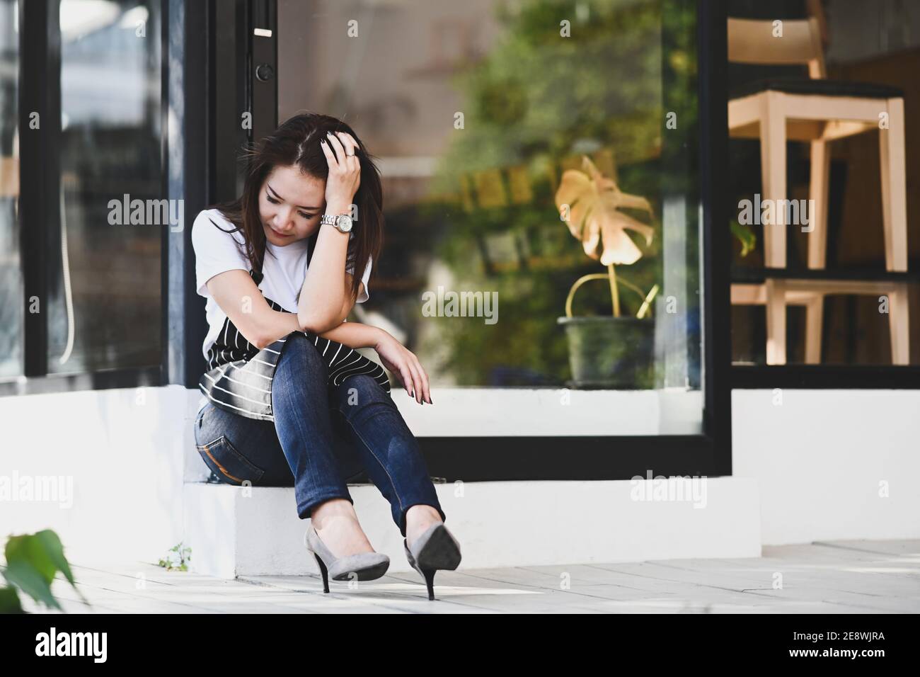 Startup small business entrepreneur woman feeling stress because of economic conditions while sitting in front of her coffee shop. Stock Photo