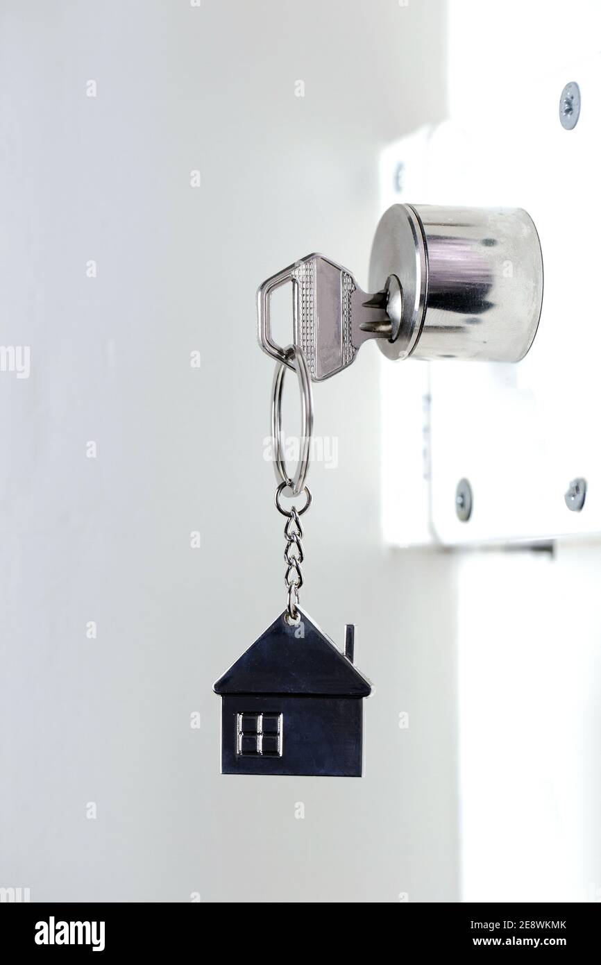 Silver house key in white door, with little keychain house, opening