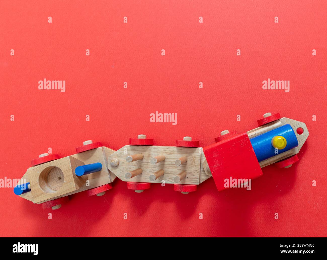 Train children toy, preschool kids game. Locomotive and carriages, wooden colorful blocks construction on red color background, top view. Stock Photo