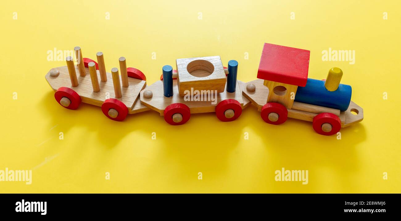 Train children toy, preschool kids game. Locomotive and carriages, wooden colorful blocks construction on yellow color background, high angle view Stock Photo